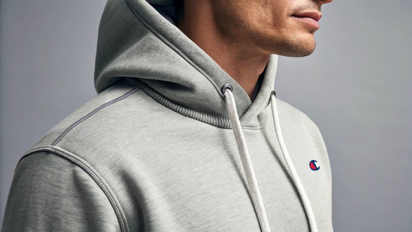 Close-up of a Champion hoodie highlighting thick cotton fabric, double-stitched seams, soft texture, and durable ribbed cuffs, set in a minimalist studio with soft lighting.
