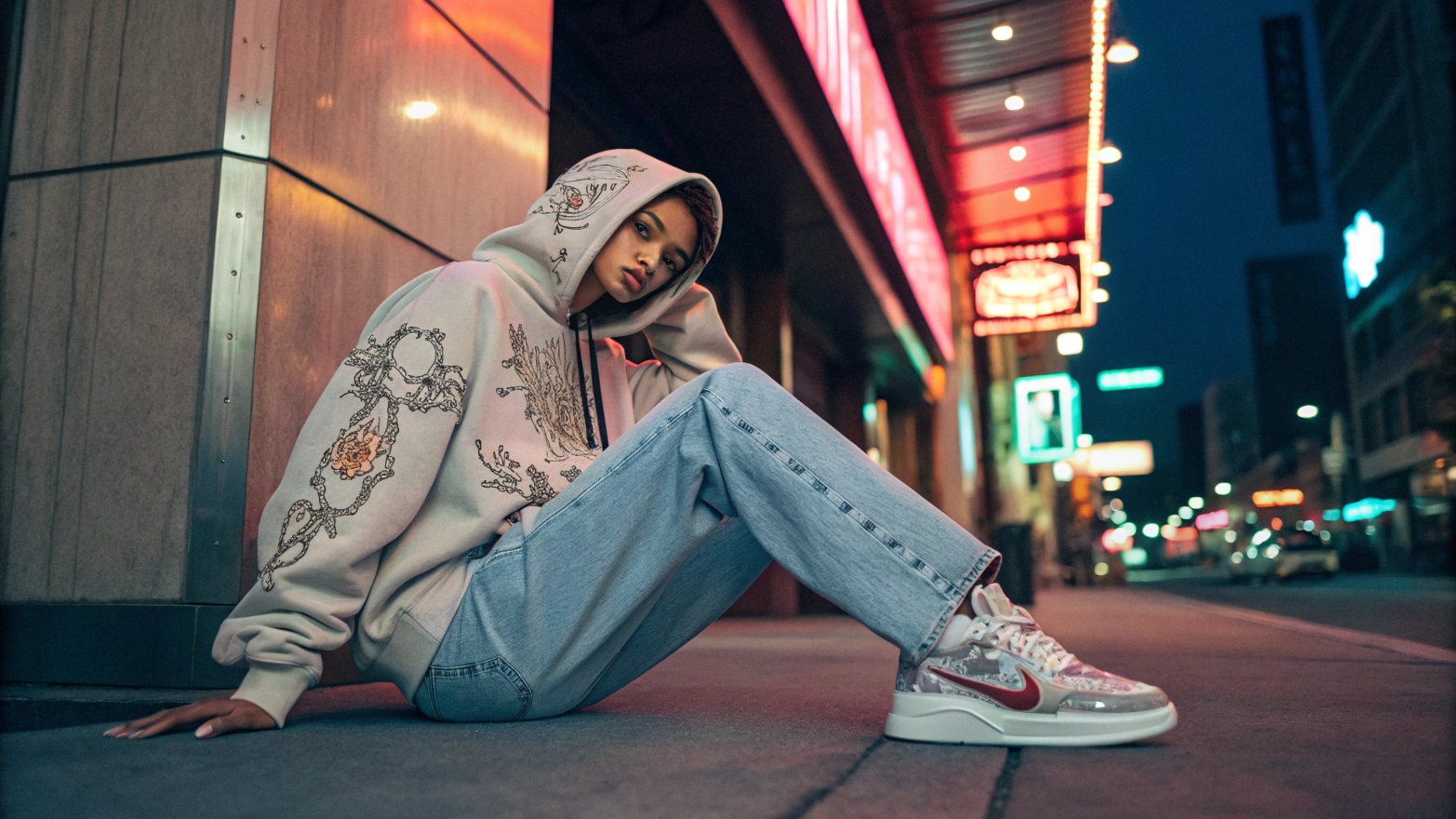 A model wearing a limited-edition Stussy x Dior collaboration outfit, featuring an oversized embroidered hoodie, relaxed-fit distressed denim, and exclusive Stussy-branded Nike sneakers, posing against a neon-lit urban backdrop.